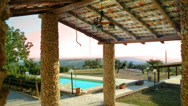 Un pilier de pierre, une piscine et une pergola décorée de guirlandes lumineuses.
