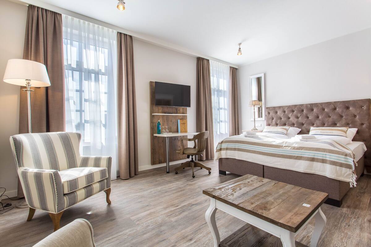 A hotel room with a bed, a desk, a chair, and a lamp.