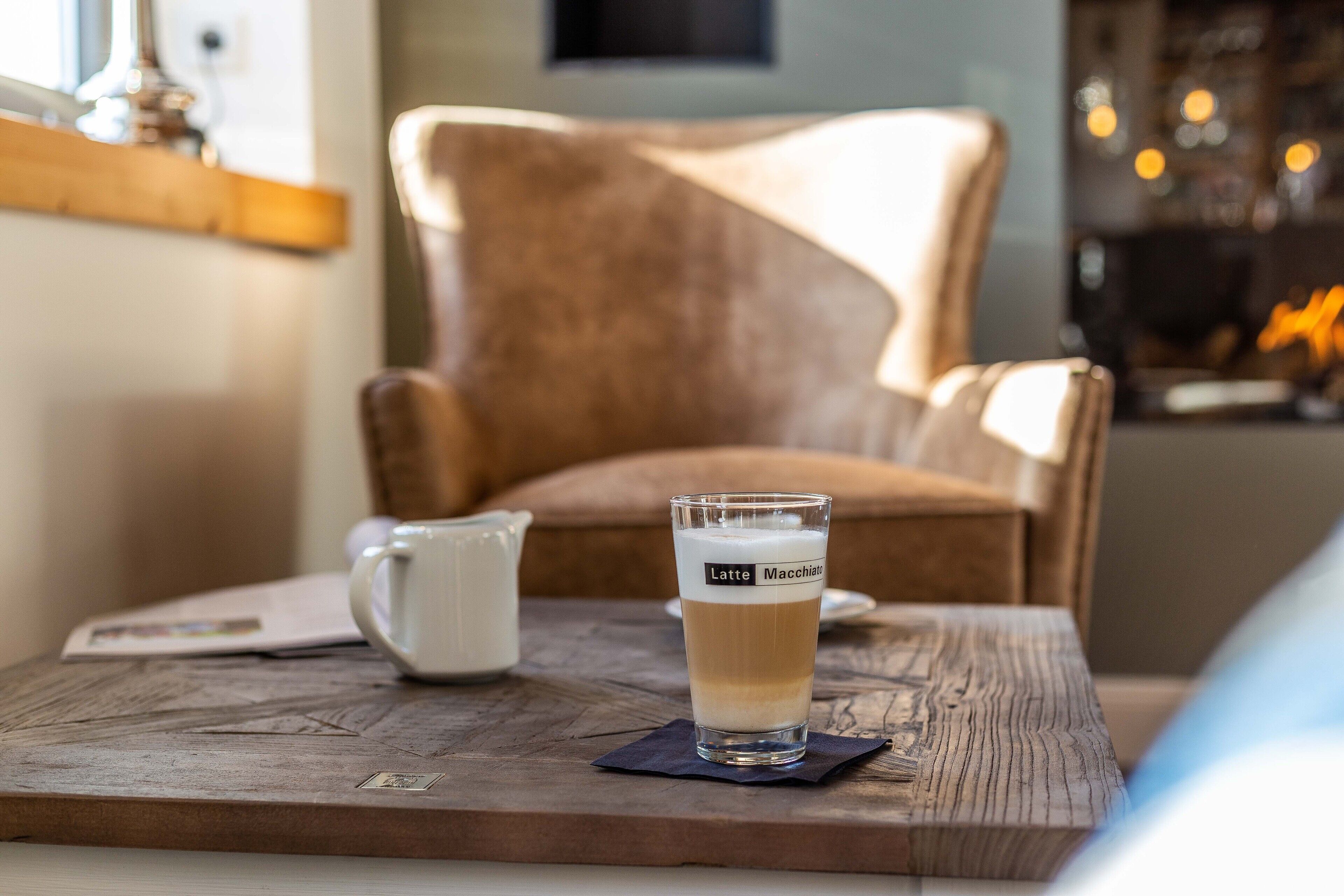 A glass of latte on a wooden table with a chair in the background.