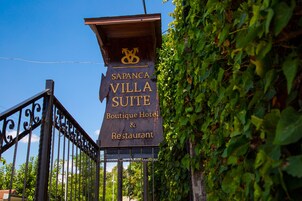 Une enseigne indiquant « Sapanca Villa Suite Boutique Hotel & Restaurant », avec une porte en fer forgé et de la verdure en arrière-plan.