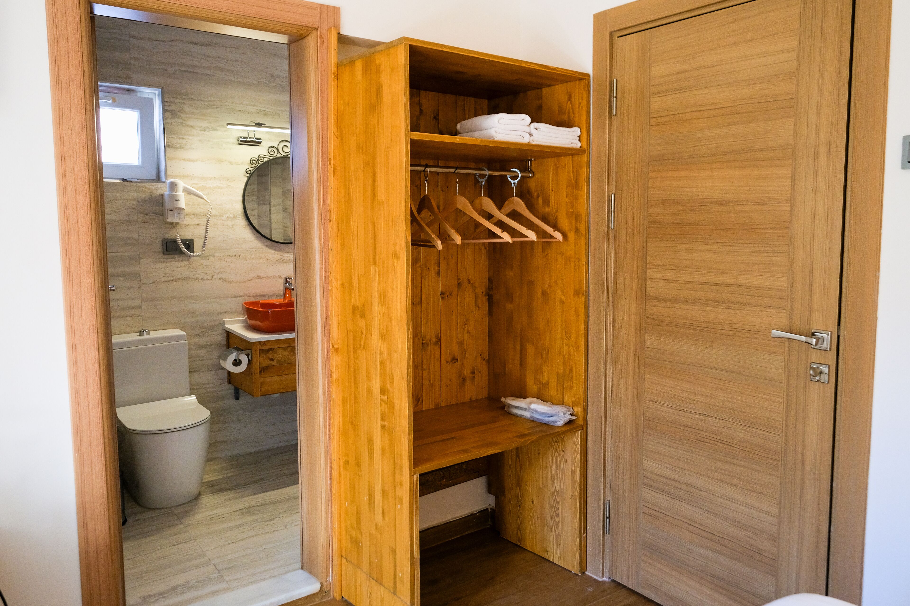 A wooden wardrobe with hanging space and shelves, a toilet, and a mirror in a bathroom.