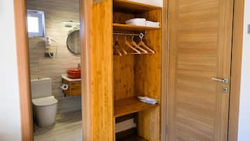 A wooden wardrobe with hanging space and shelves, a toilet, and a mirror in a bathroom.