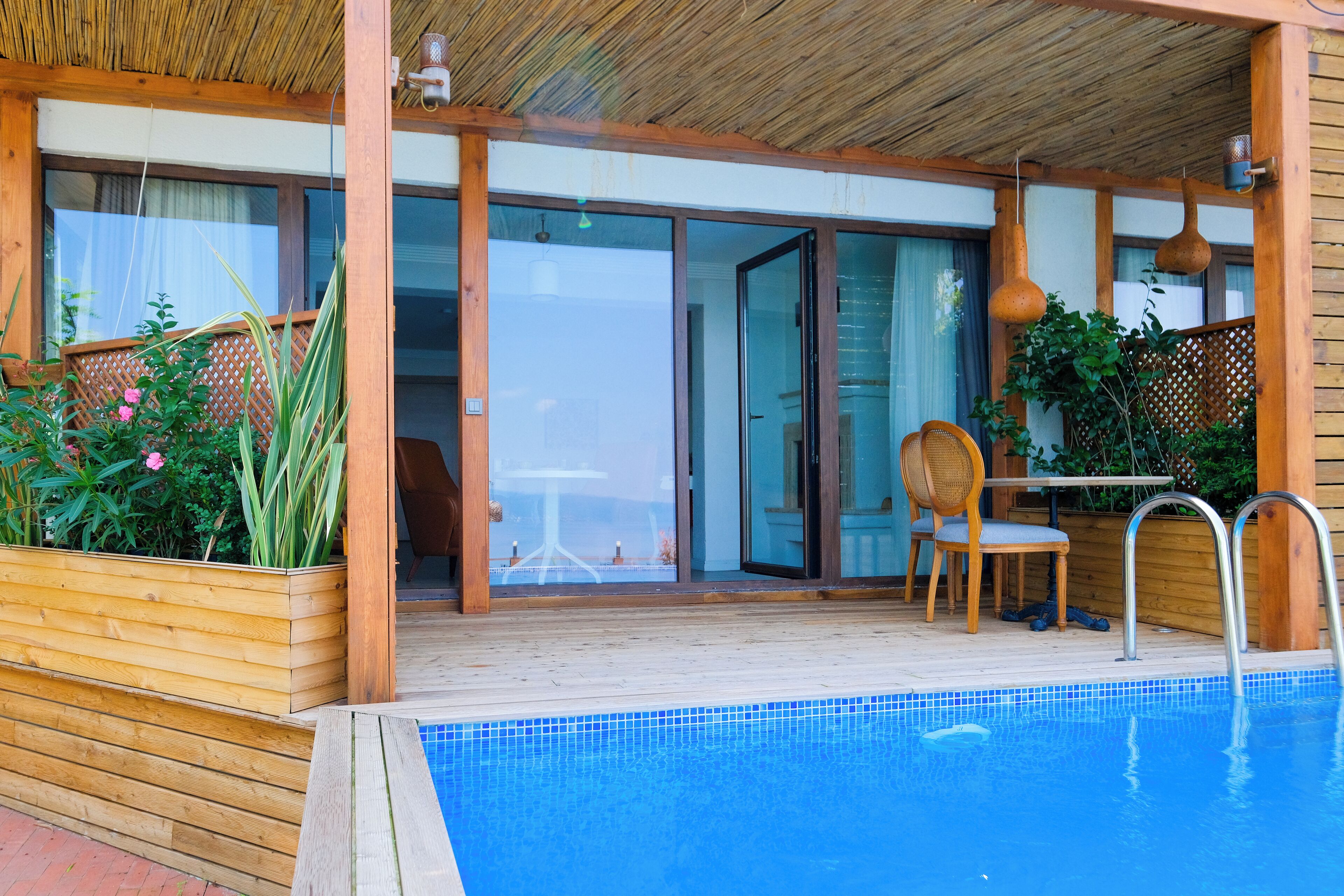 A pool area with a wooden deck, a glass door leading to a room, and a chair by the pool.