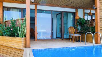 A pool area with a wooden deck, a glass door leading to a room, and a chair by the pool.