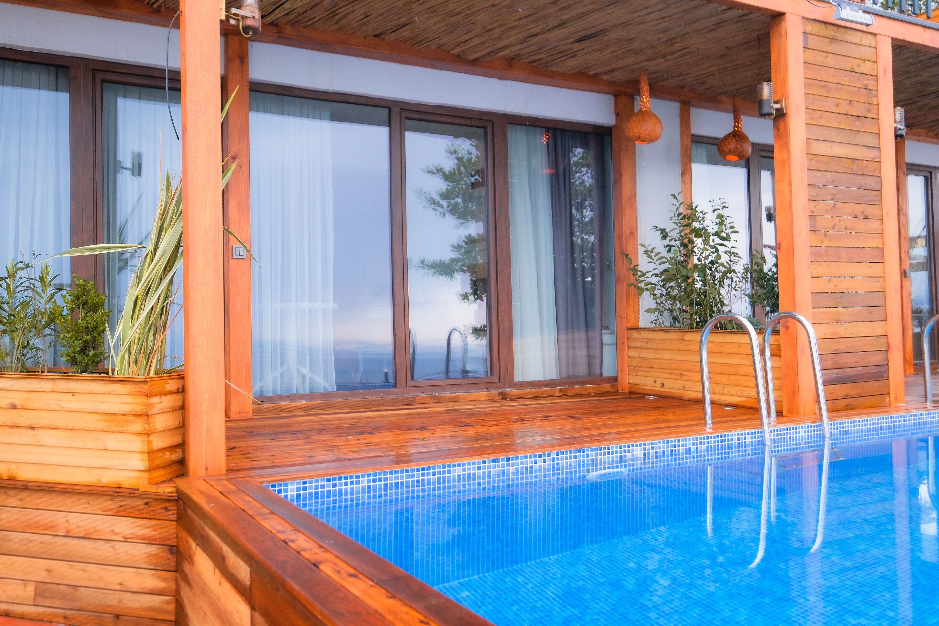 Um deck de madeira com piscina, corrimãos de madeira e plantas em vasos.