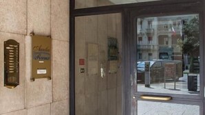 Entrada de un hotel con puerta de cristal, una placa en la pared y vista de la calle.