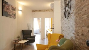 Una sala de estar con pared de ladrillo, un ventanal y una puerta que da a otra habitación.