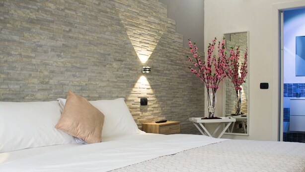 Un dormitorio moderno con pared de ladrillo visto, una mesita de noche con un florero de flores rosas y un espejo grande.
