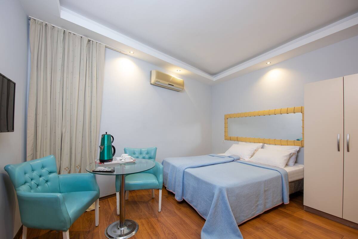 A hotel room with a bed, two chairs, a small table, a TV, and a wardrobe.