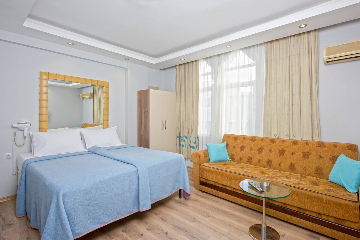 A hotel room with a bed, a sofa, a mirror, a wardrobe, and a window with curtains.