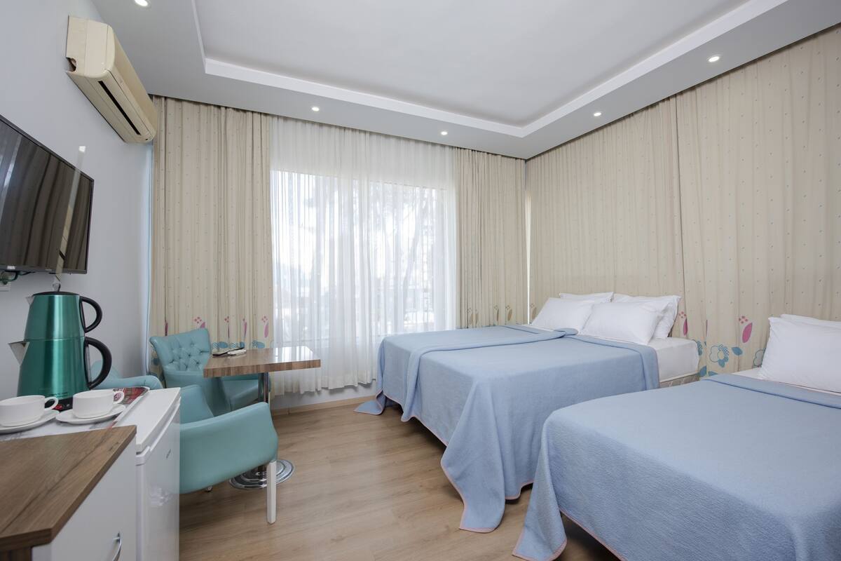 A hotel room with two beds, a desk with a kettle, a chair, and a TV mounted on the wall.