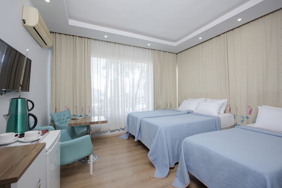 A hotel room with two beds, a small table, a chair, a TV, and an air conditioning unit.