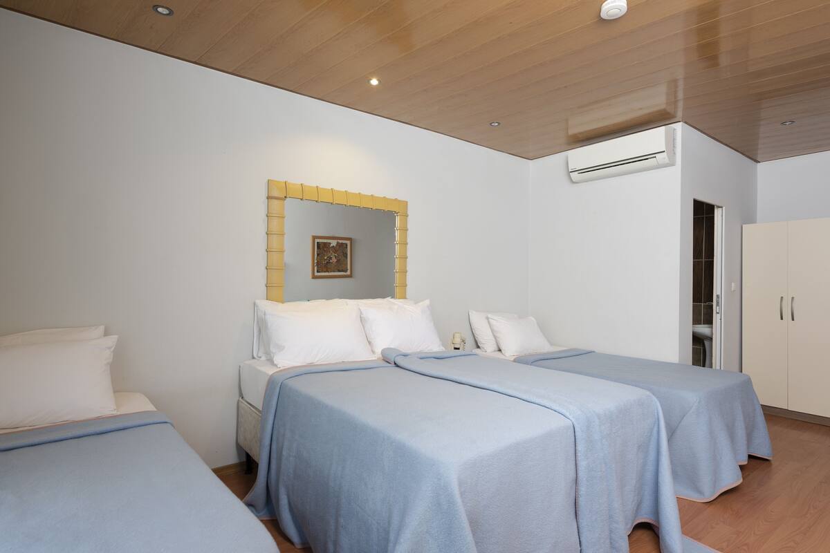 A hotel room with two beds, a wooden ceiling, an air conditioning unit, and a wardrobe.