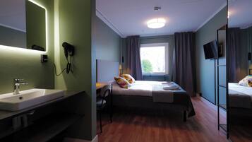 Una habitación de hotel con un espejo grande, una cama con almohadas coloridas, una mesita de noche con una lámpara y una ventana con cortinas.