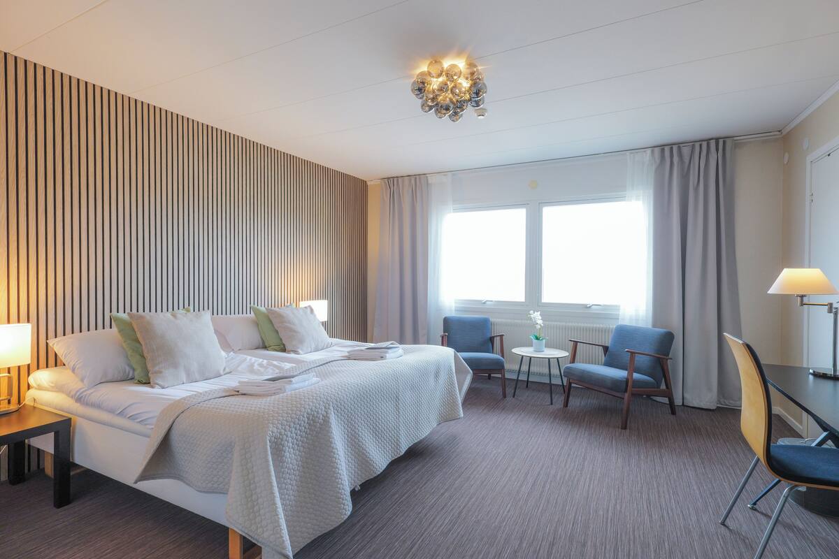 Una habitación de hotel con cama, dos sillas, una mesita y una lámpara.