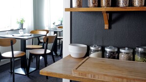 Ein moderner Essbereich mit einem Holztisch und Stühlen, einer Kühlpflanze und einer Küchenzeile mit Gläsern voller Getreide und Gewürzen.