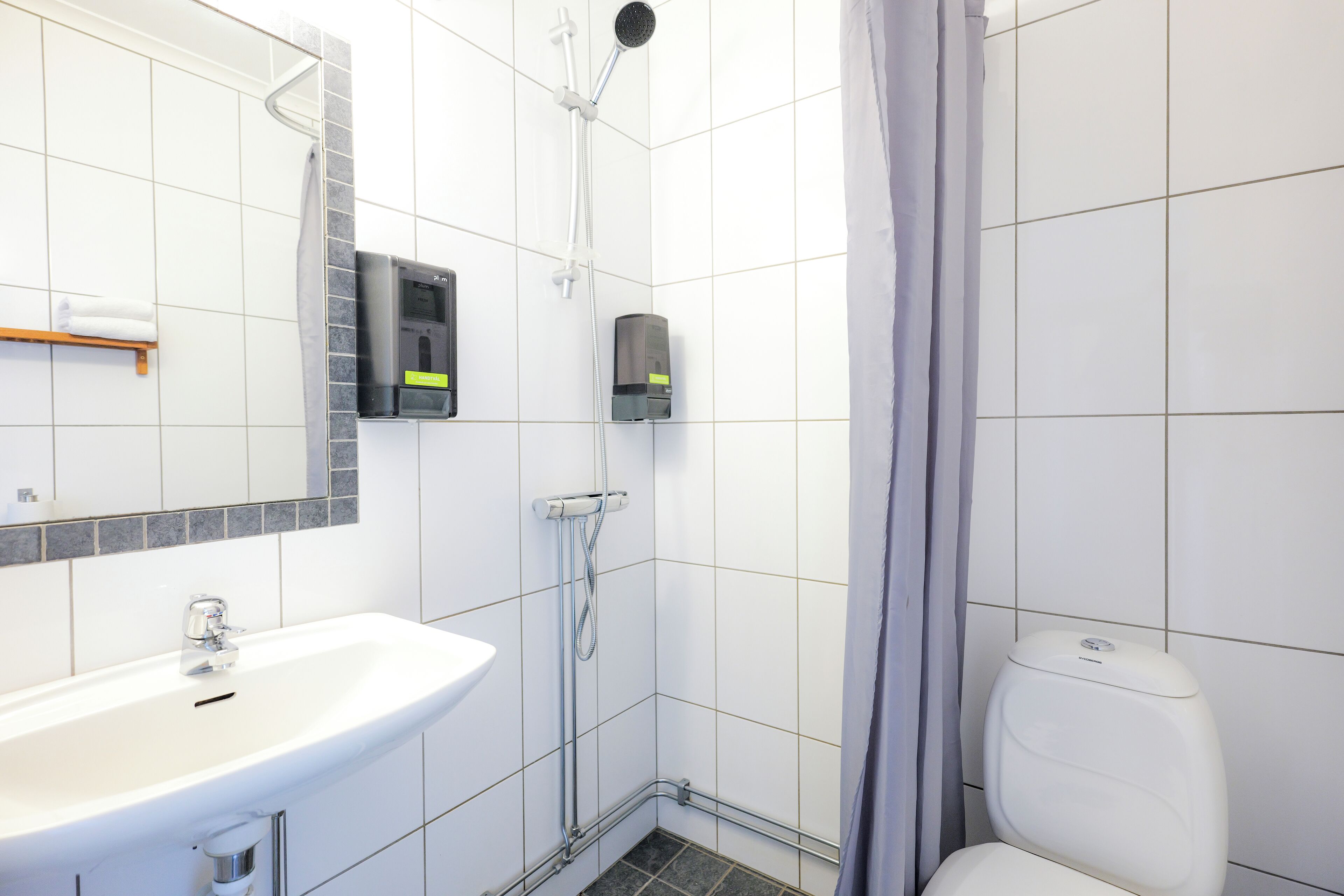 Een badkamer met een witte wastafel, een spiegel, een douche en een toilet.