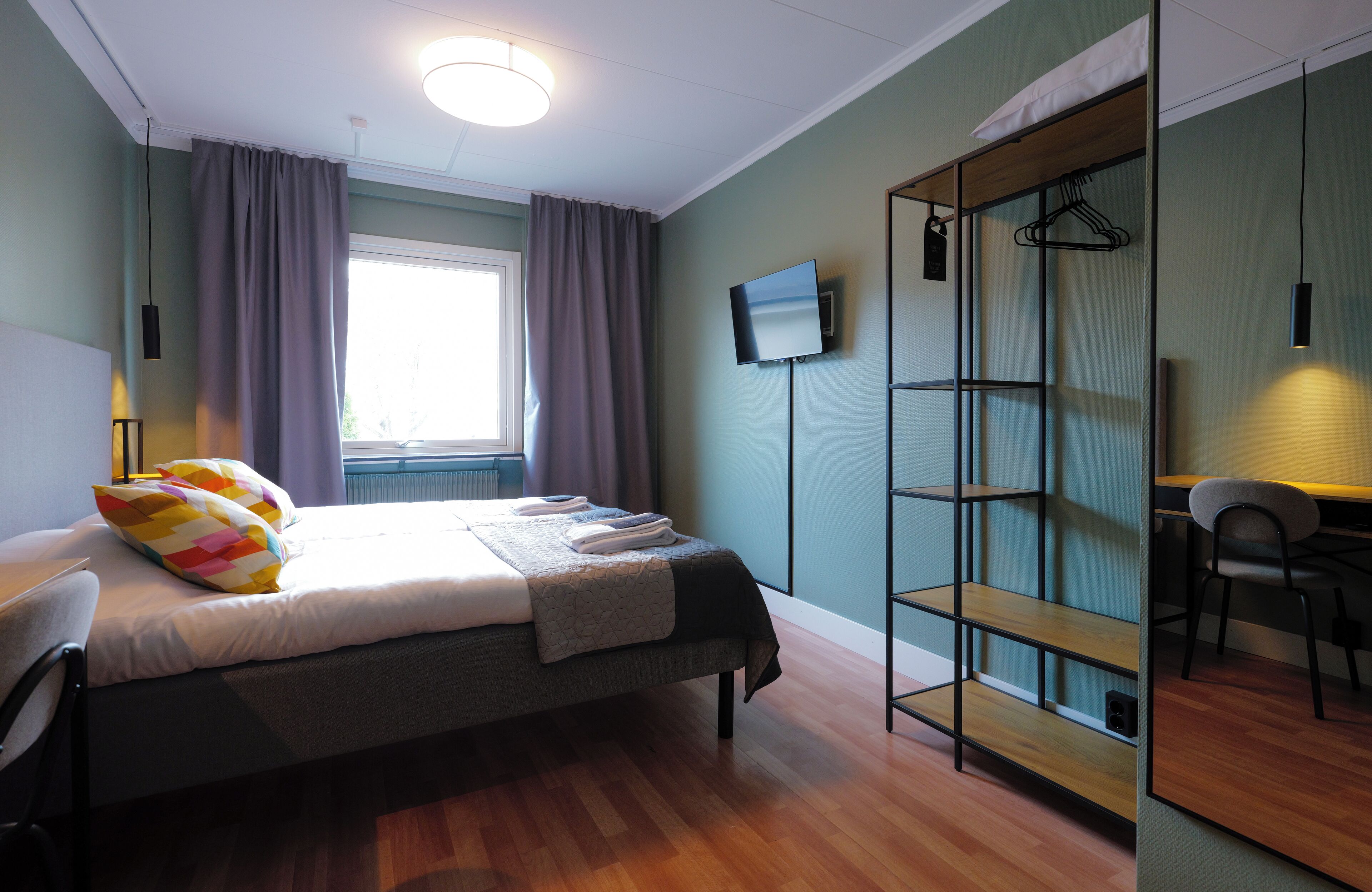 Een slaapkamer met een bed, een bureau, een stoel, een televisie en een kledingkast.