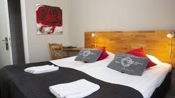 Habitación de hotel con una cama grande, dos almohadas, cabecera de madera, un escritorio y una silla.