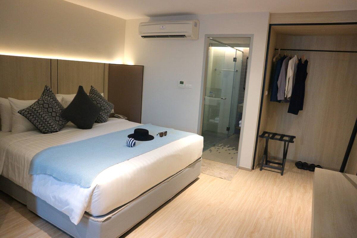 A hotel room with a bed, a bedside table, a hanging coat rack, and a bathroom door.