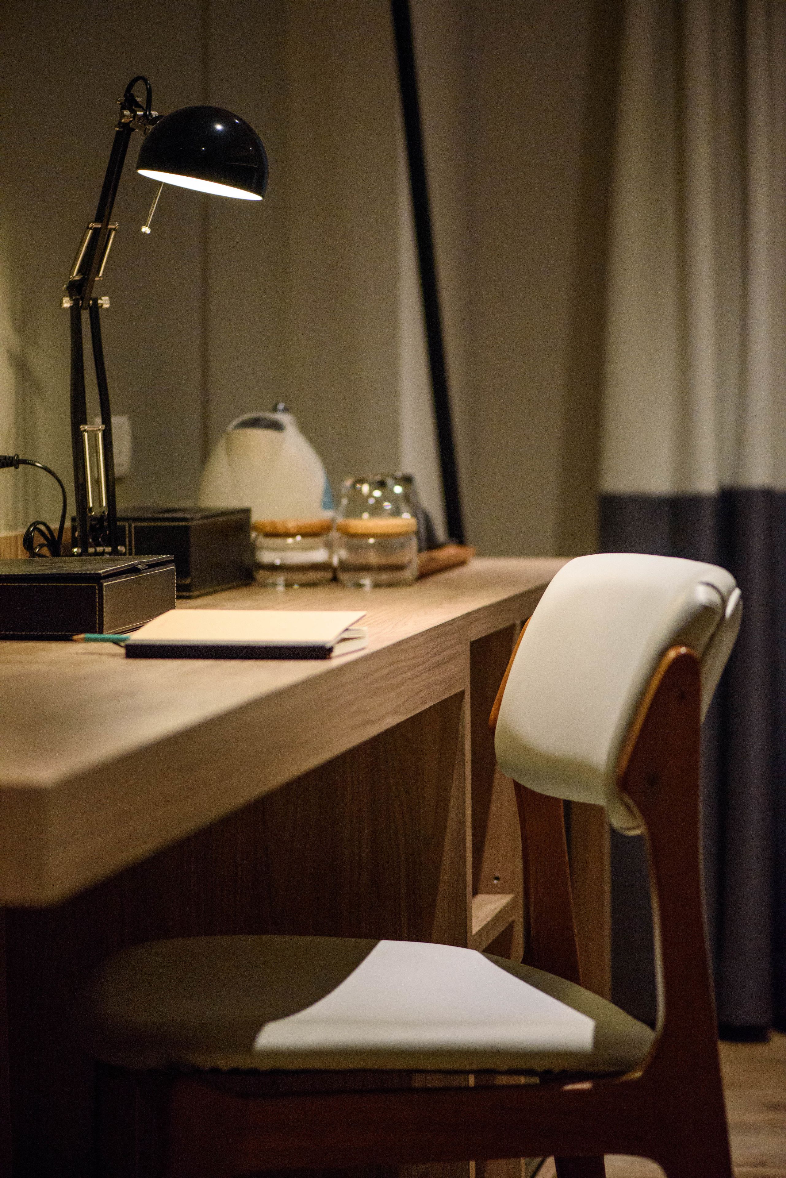 Een houten bureau met een zwarte bureaulamp, een witte stoel en een notitieboekje.