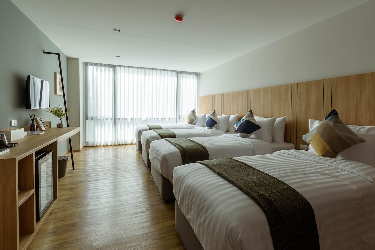 A hotel room with three beds, a desk with a computer, and a large window with curtains.