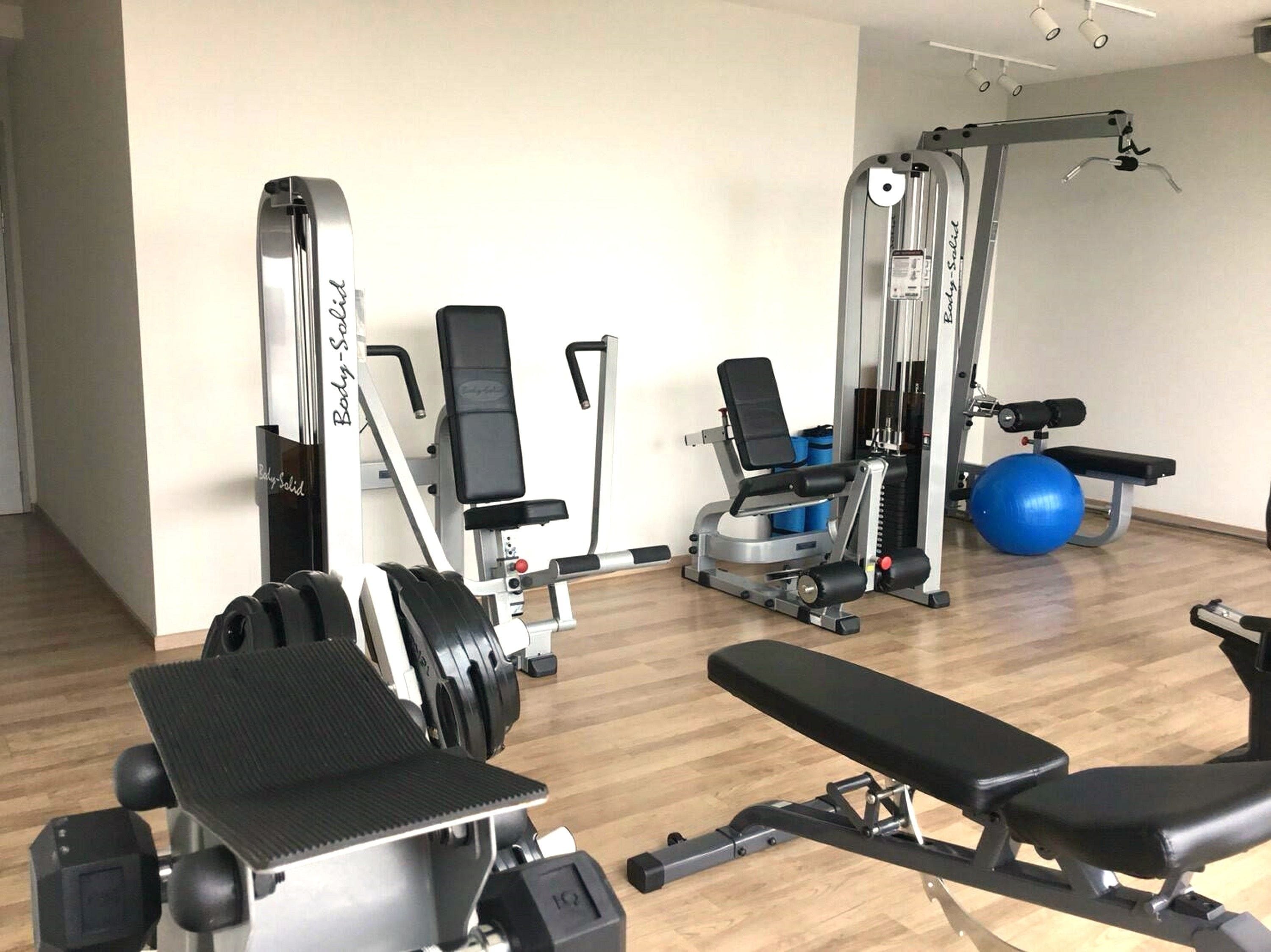 Un gimnasio con máquinas de pesas, una banca y pelotas de ejercicio.