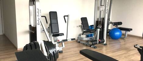 Un gimnasio con máquinas de pesas, una banca y pelotas de ejercicio.
