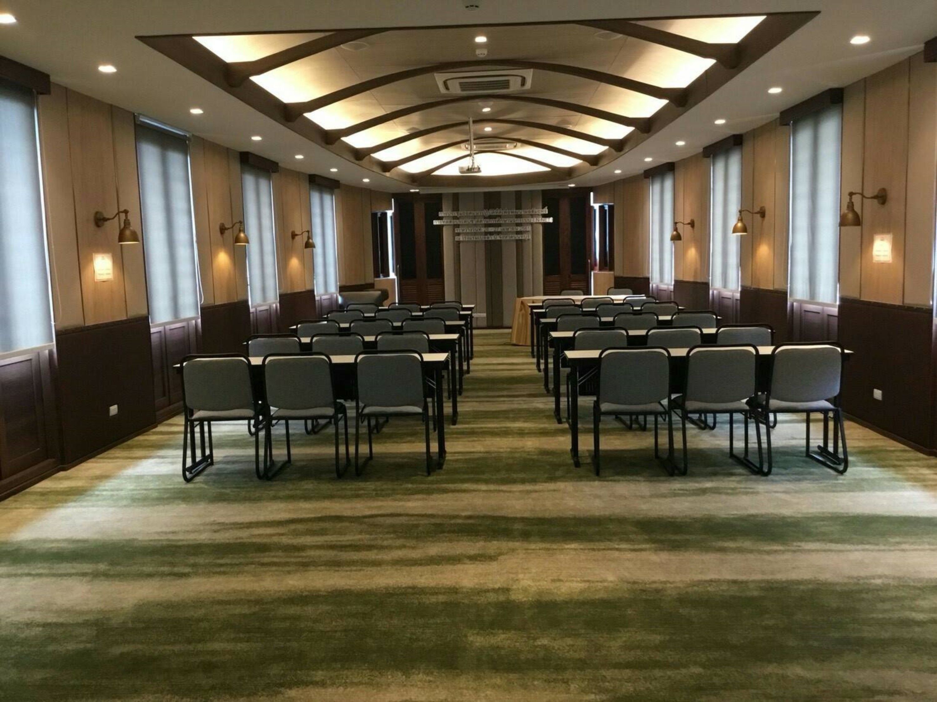 A conference room with rows of tables and chairs, recessed lighting, and a carpeted floor.