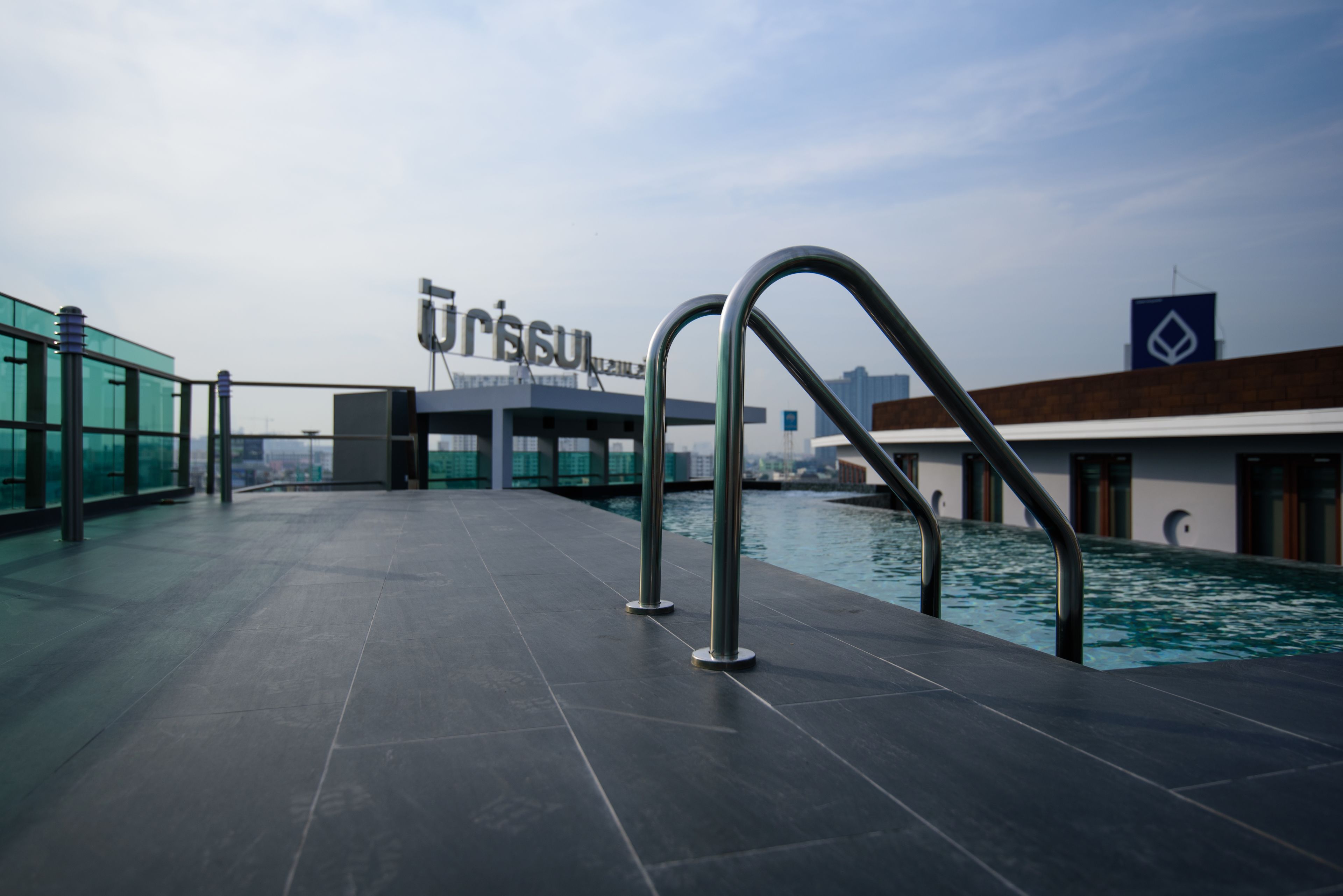 Un espace piscine sur le toit, doté d’un design moderne, comprenant une rambarde en verre et des échelles métalliques pour accéder à la piscine.