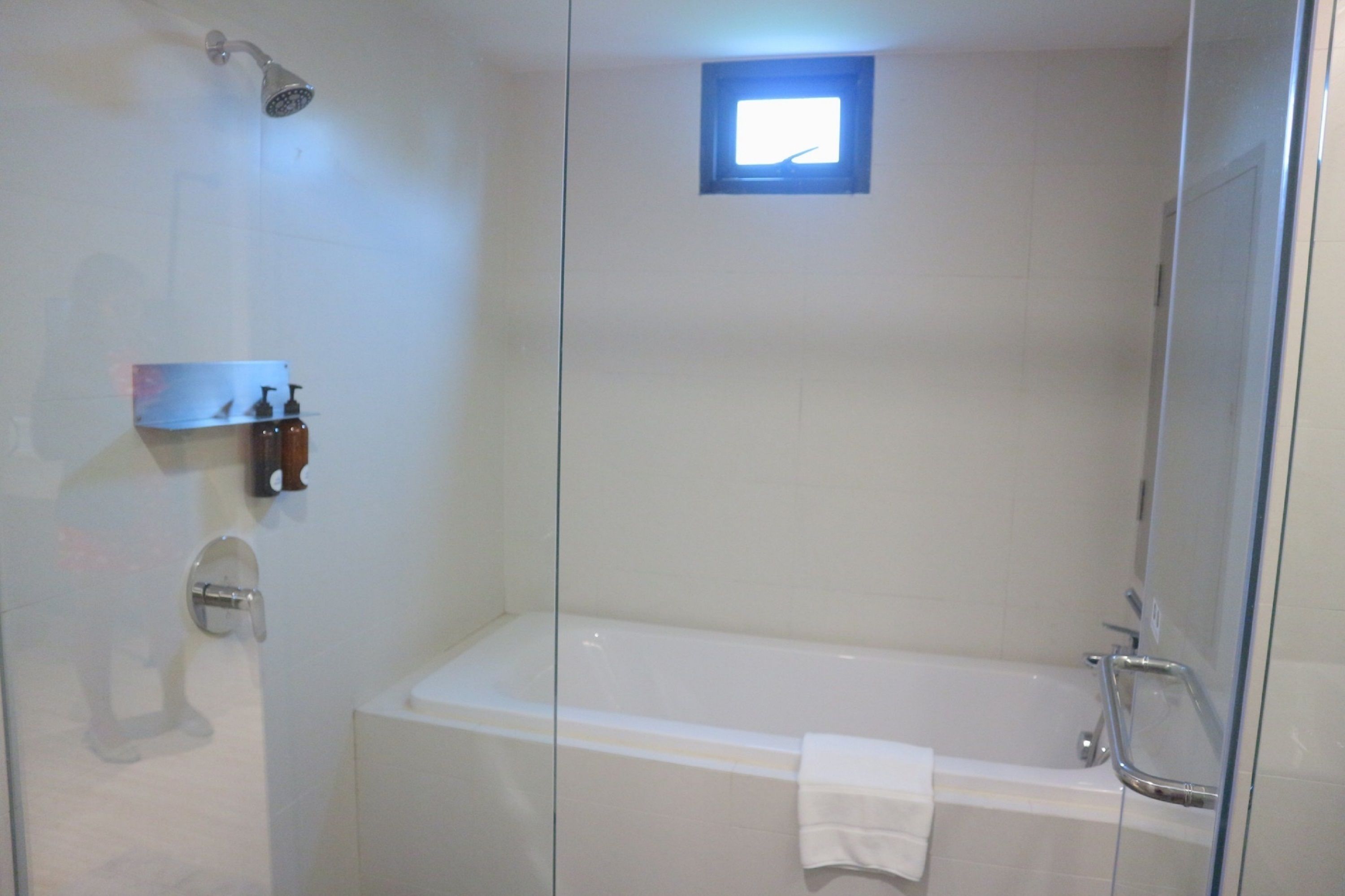 Een moderne badkamer met een douchecabine van glas, een witte badkuip en een klein raam voor daglicht.