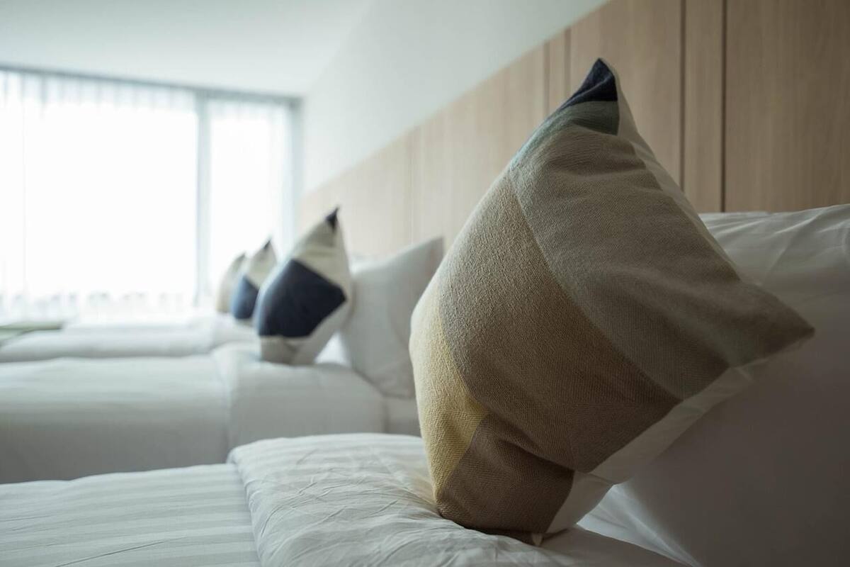 A hotel room with a bed, pillows, and a wooden headboard.