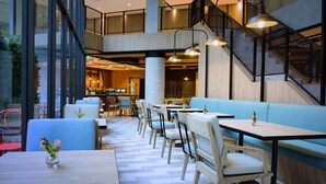 Un comedor interior moderno con techos altos, una escalera central y una variedad de opciones de asientos, incluyendo mesas y cabinas.