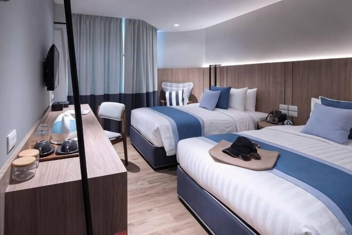 A hotel room with two beds, a desk with a chair, a TV, and a window with curtains.