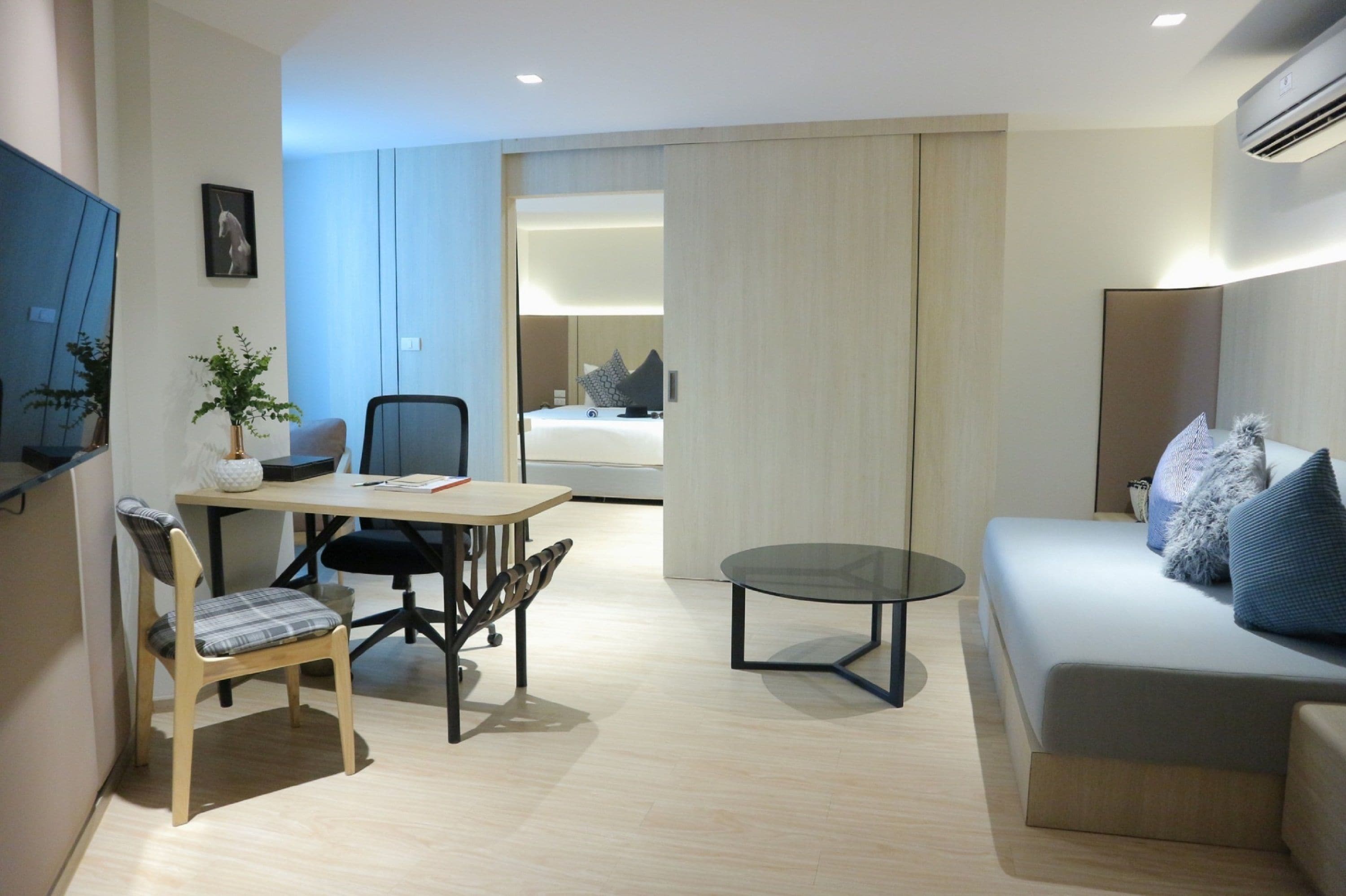 A modern hotel room with a dining area, a sofa, a TV, and a bed.