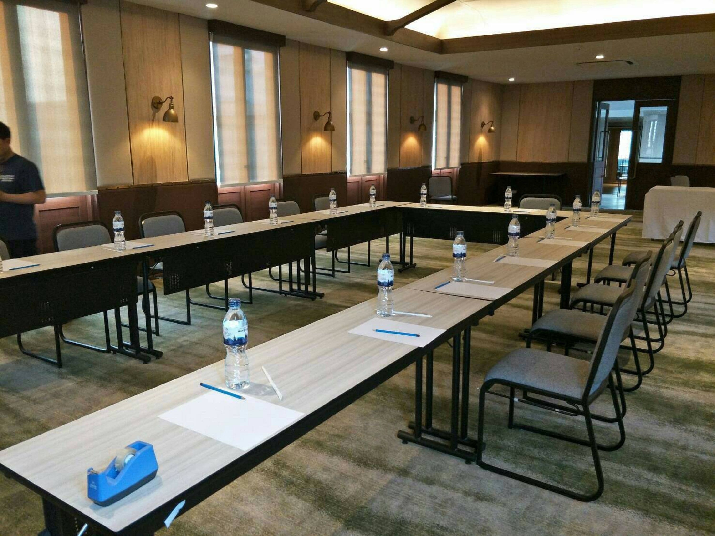 Une salle de conférence avec de longues tables, des chaises, des bouteilles d’eau et un distributeur de ruban adhésif.