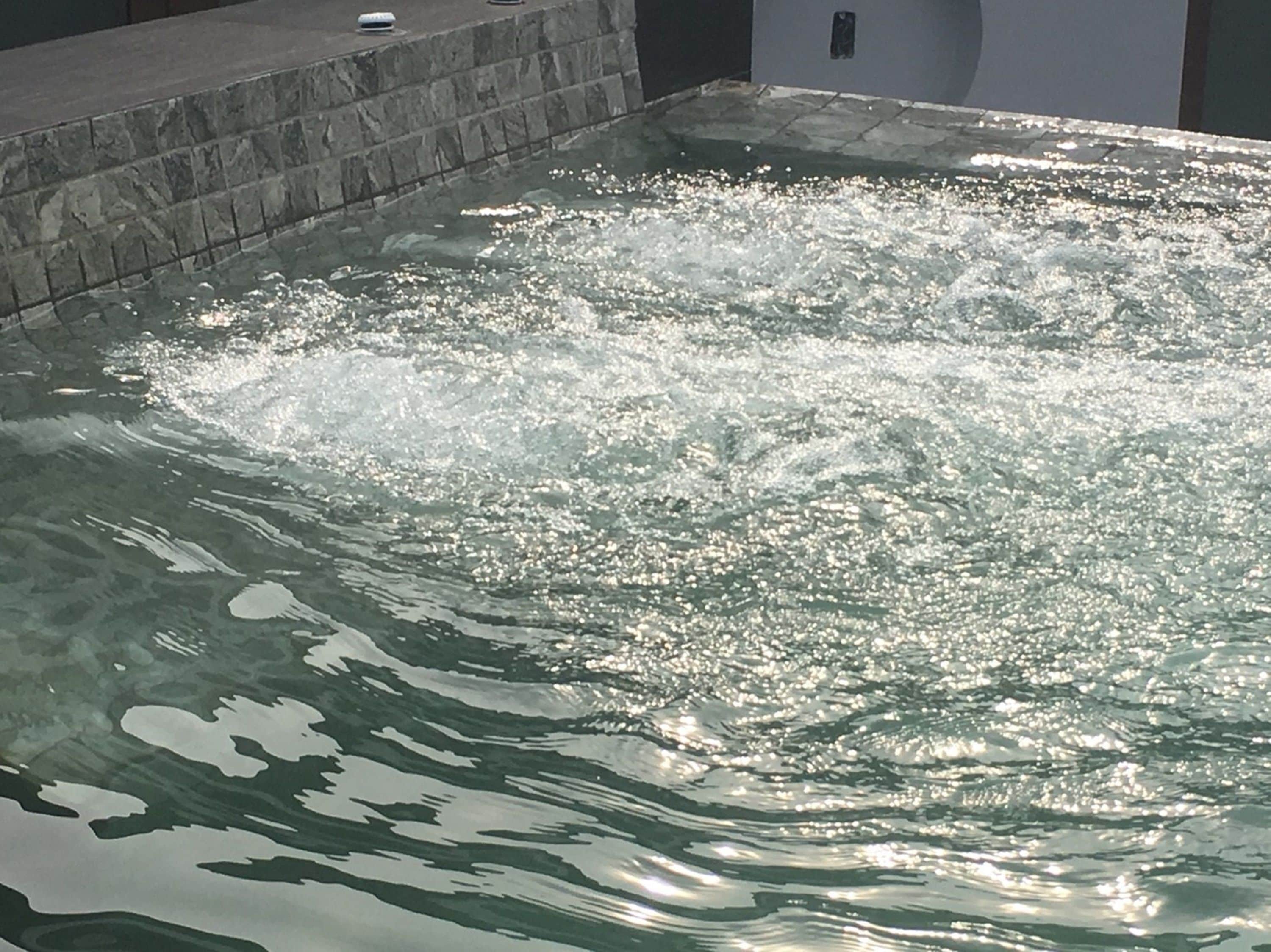 Un bain à remous où l’eau éclabousse, entouré de carreaux de pierre et bordé de béton.