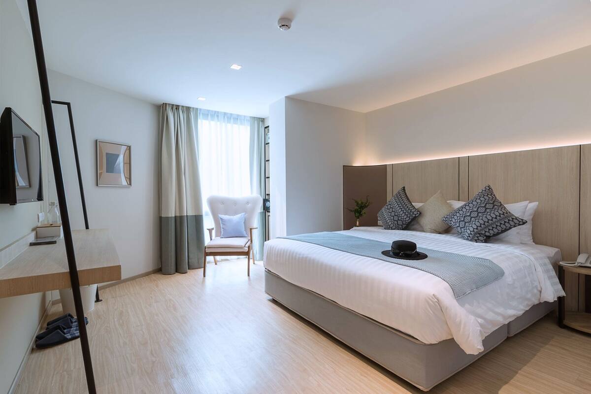 A modern hotel room with a large bed, a chair, a bedside table, and a TV.