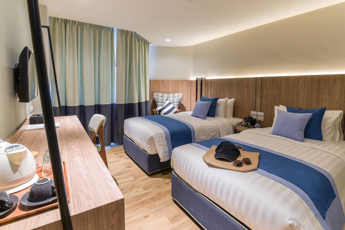 A hotel room with two beds, a desk with a chair, a television, and a window with curtains.