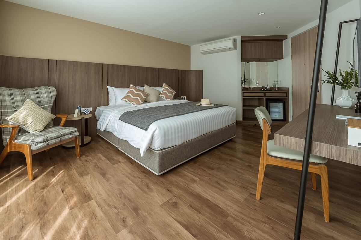 A modern bedroom with a large bed, a wooden headboard, a bedside table, a chair, a desk, and a mirror.