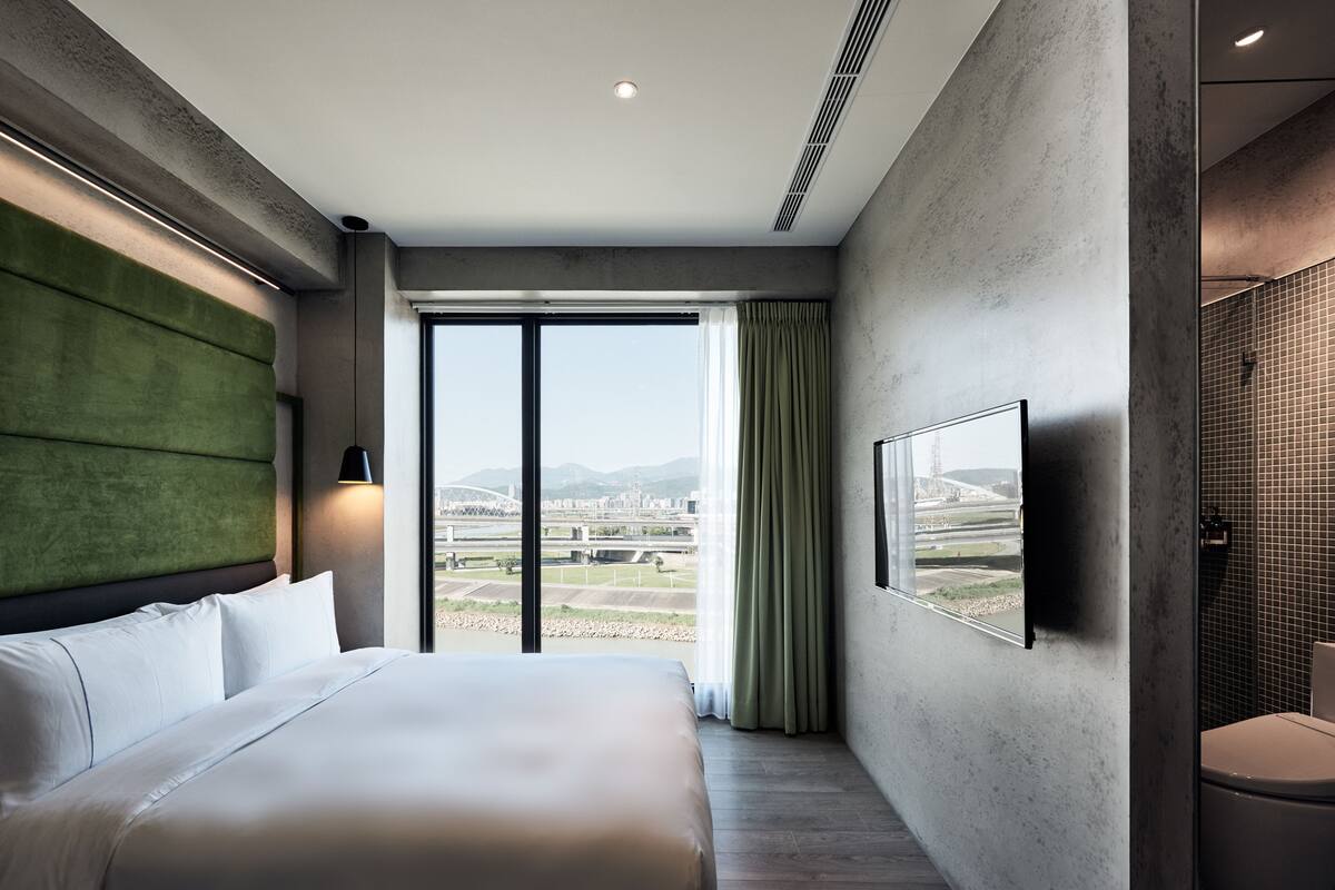 Una habitación de hotel moderna con una cama grande, vistas a la ciudad y un baño con pared de azulejos.