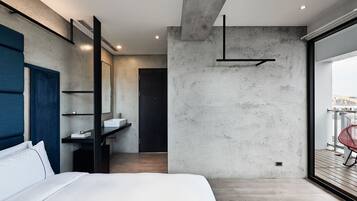 Un dormitorio moderno con una cama grande, un baño con lavamanos y vistas a la ciudad a través de un ventanal.