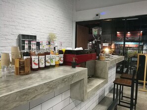 A bar area with a white brick wall, a coffee machine, and various bottles of liquor. - Backpack Station - Hostel (Bangkok)