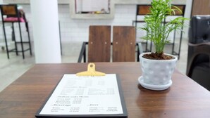 Un menú sujeto a un portapapeles sobre una mesa de madera, con una planta en maceta al lado.