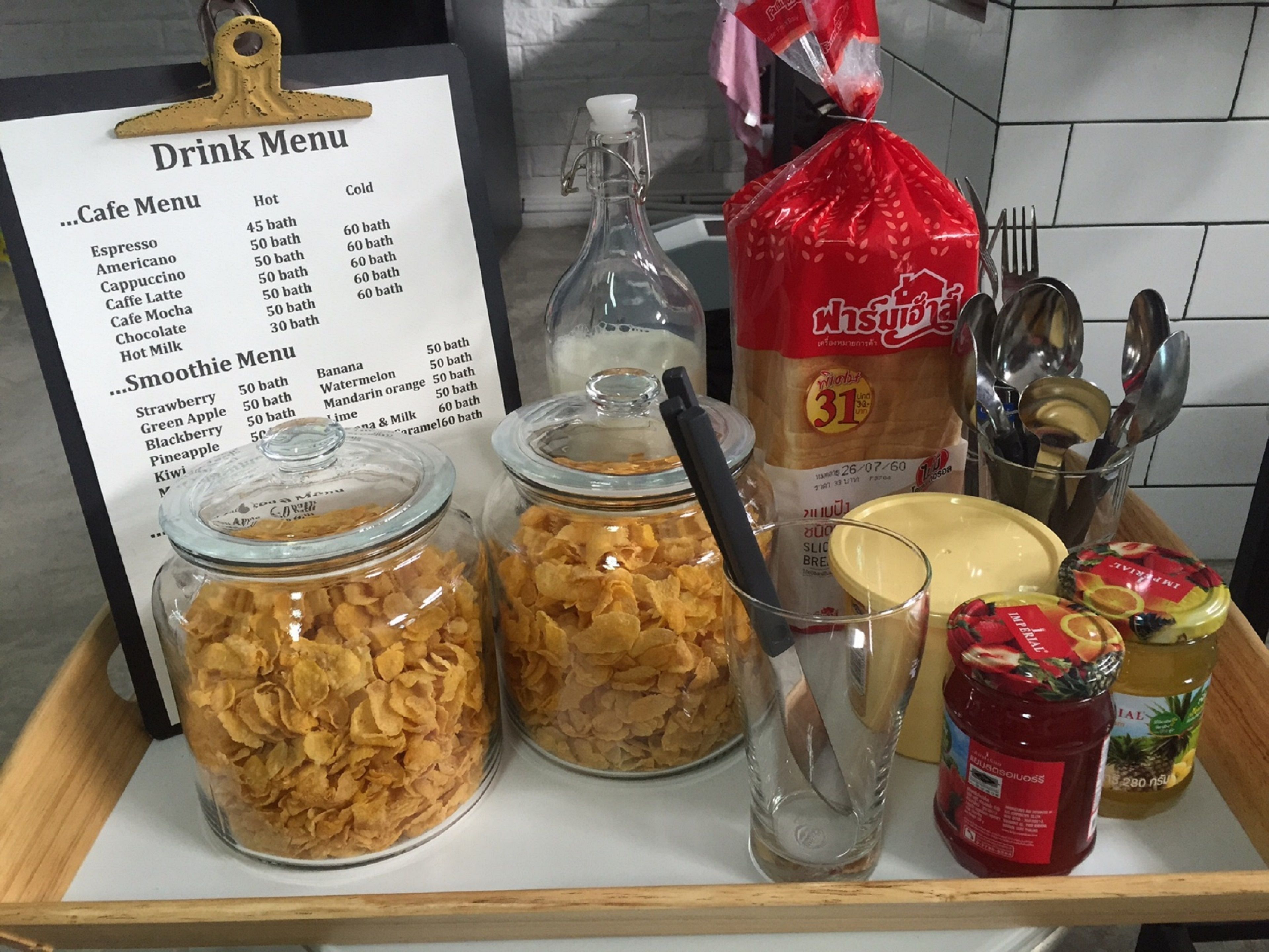 Una bandeja con un menú de bebidas, frascos de cereal, condimentos y una botella de sirope.