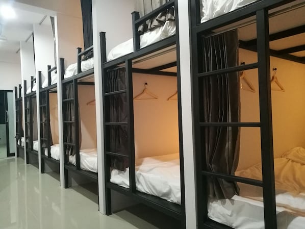 Varias literas con estantes de almacenamiento y espacio para colgar, en una habitación luminosa con piso de baldosas.