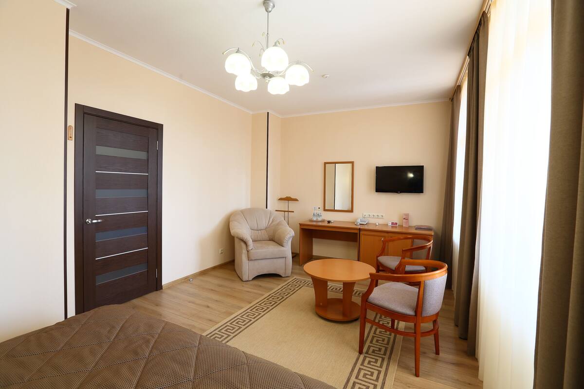 A hotel room with a bed, a desk, a chair, a TV, and a window with curtains.