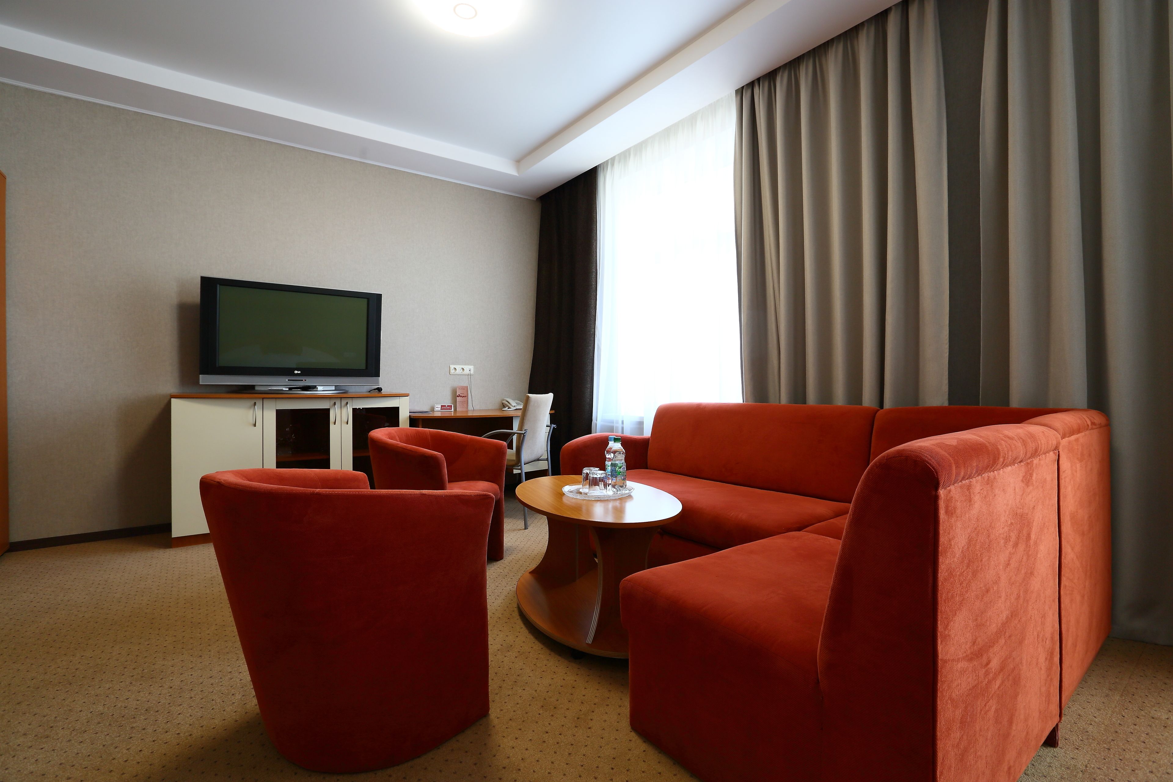 Hotellihuone, jossa on punainen sohva, pieni pyöreä pöytä, televisio ja kaappi.