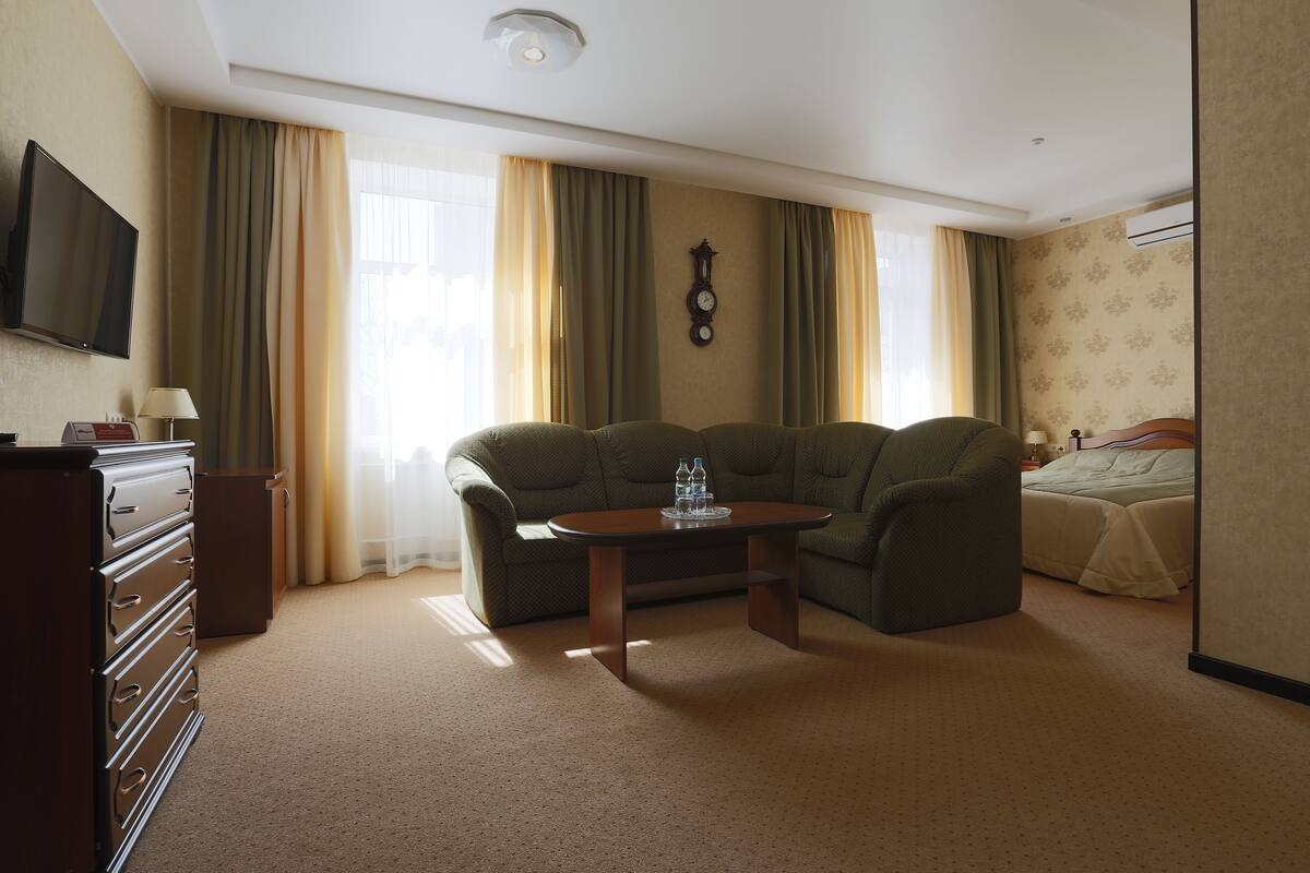 A hotel room with a sofa, a small table, a TV, a dresser, and a bed.