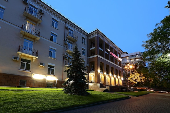 Un hôtel à plusieurs étages, doté de balcons, d’une entrée bien éclairée et d’une cour dallée.